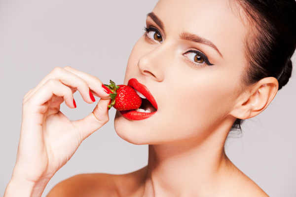 Brunette model with red lip blushing biting a strawberry